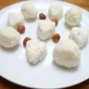 Keto coconut fat bombs in round and heart shapes on a white plate with hazelnuts.