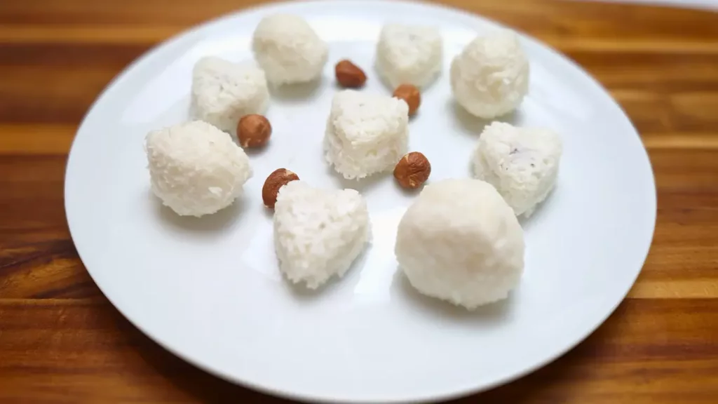 Keto coconut fat bombs in round and heart shapes on a white plate with hazelnuts.