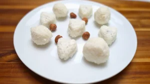 Keto coconut fat bombs in round and heart shapes on a white plate with hazelnuts.
