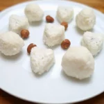 Keto coconut fat bombs in round and heart shapes on a white plate with hazelnuts.