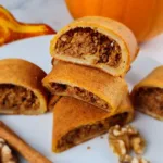A plate of keto pumpkin pinwheels (keto tikvenik) with walnuts and cinnamon sticks on a white plate