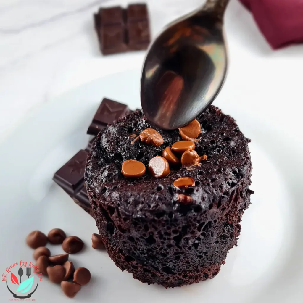 A flourless brownie in a mug cake on a white plate with chocolate chunks and chocolate chips on top.