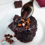 A flourless brownie in a mug cake on a white plate with chocolate chunks and chocolate chips on top.