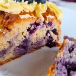 A close-up view of a slice of keto blueberry creme fraiche pound cake topped with keto Royal Icing Buttercream, showcasing the rich texture and blueberries embedded within.