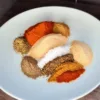 Keto Cajun Seasoning ingredients, including salt, garlic powder, onion powder, paprika, oregano, thyme, black pepper, cumin, coriander, and cayenne pepper, in a white bowl on a dark table.