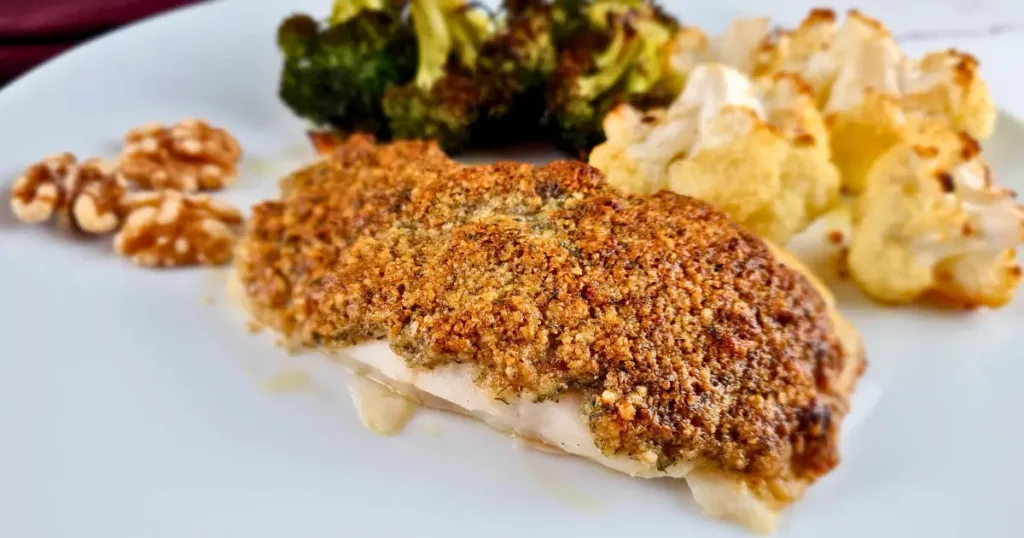 A close-up image of a keto Mediterranean cod with a walnut crust, served with roasted vegetables and walnuts on a white plate.
