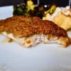 A close-up image of a keto Mediterranean cod with a walnut crust, served with roasted vegetables and walnuts on a white plate.
