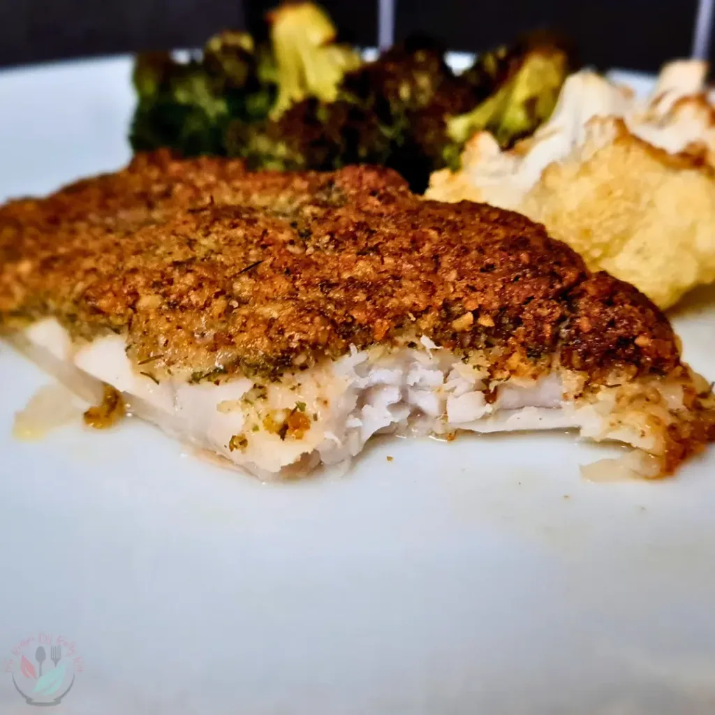 A close-up image of a keto Mediterranean cod with a walnut crust, served with roasted vegetables and walnuts on a white plate.