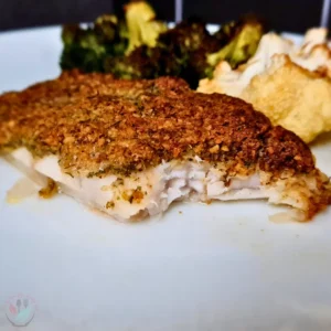 A close-up image of a keto Mediterranean cod with a walnut crust, served with roasted vegetables and walnuts on a white plate.