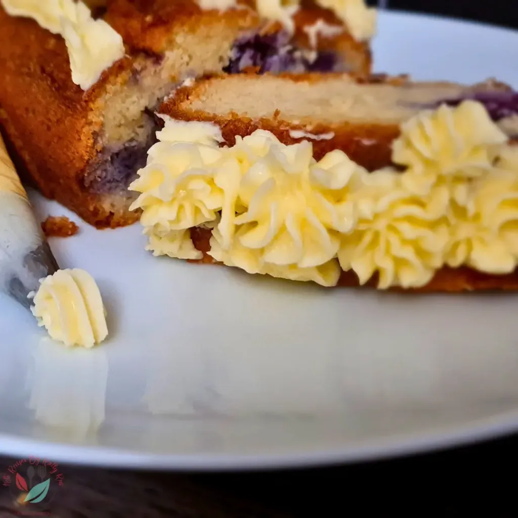 A slice of keto royal icing buttercream cake with sugar-free frosting, showcasing layers of cake and purple filling, adorned with intricate piped buttercream decorations, placed on a white plate.