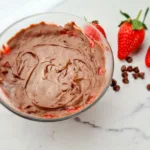 A Keto Mug Cheesecake with chocolate and strawberry jam, fresh strawberries, and chocolate chips on a marble surface.