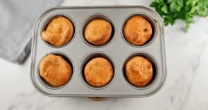 A top view of six golden brown Yorkshire puddings made with almond flour, sitting in a grey baking tray, showcasing a gluten-free option for this classic dish.