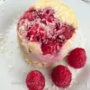 A delicious keto mug cake made with coconut flour and topped with raspberries and shredded coconut, presented on a white plate beside a mug with “Have A Break” text and a donut image, showcasing a tasty yet healthy dessert option.