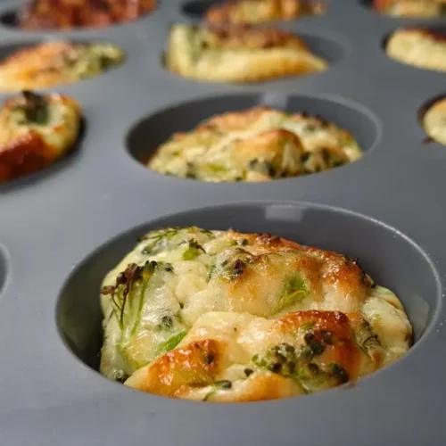 A tray of freshly baked cottage cheese egg muffins with pancetta, showing the golden-brown tops and visible bits of green herbs.