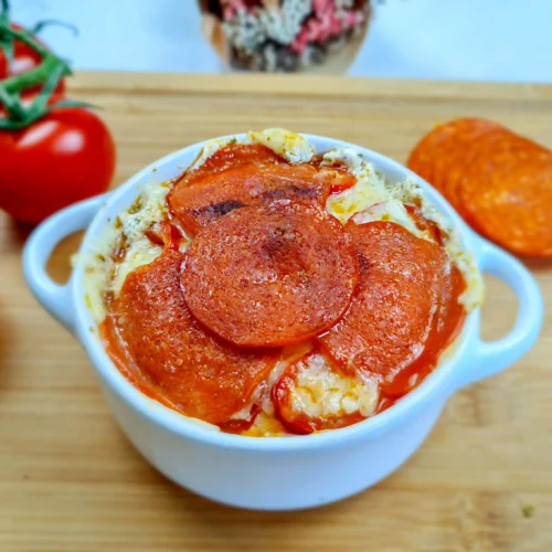 Delicious keto-friendly Cottage Cheese Pizza Bowl topped with savory pepperoni slices, garnished with fresh herbs, and served in a white bowl on a rustic wooden table, ready to enjoy.