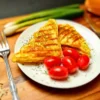 “Delicious keto-friendly Chaffwich featuring a golden-brown chaffle heart, layered with pepperoni, on a rustic wooden plate garnished with cherry tomatoes and a sprinkle of shredded cheese, hinting at the fresh ingredients used in its creation.