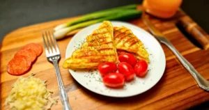 “Delicious keto-friendly Chaffwich featuring a golden-brown chaffle heart, layered with pepperoni, on a rustic wooden plate garnished with cherry tomatoes and a sprinkle of shredded cheese, hinting at the fresh ingredients used in its creation.