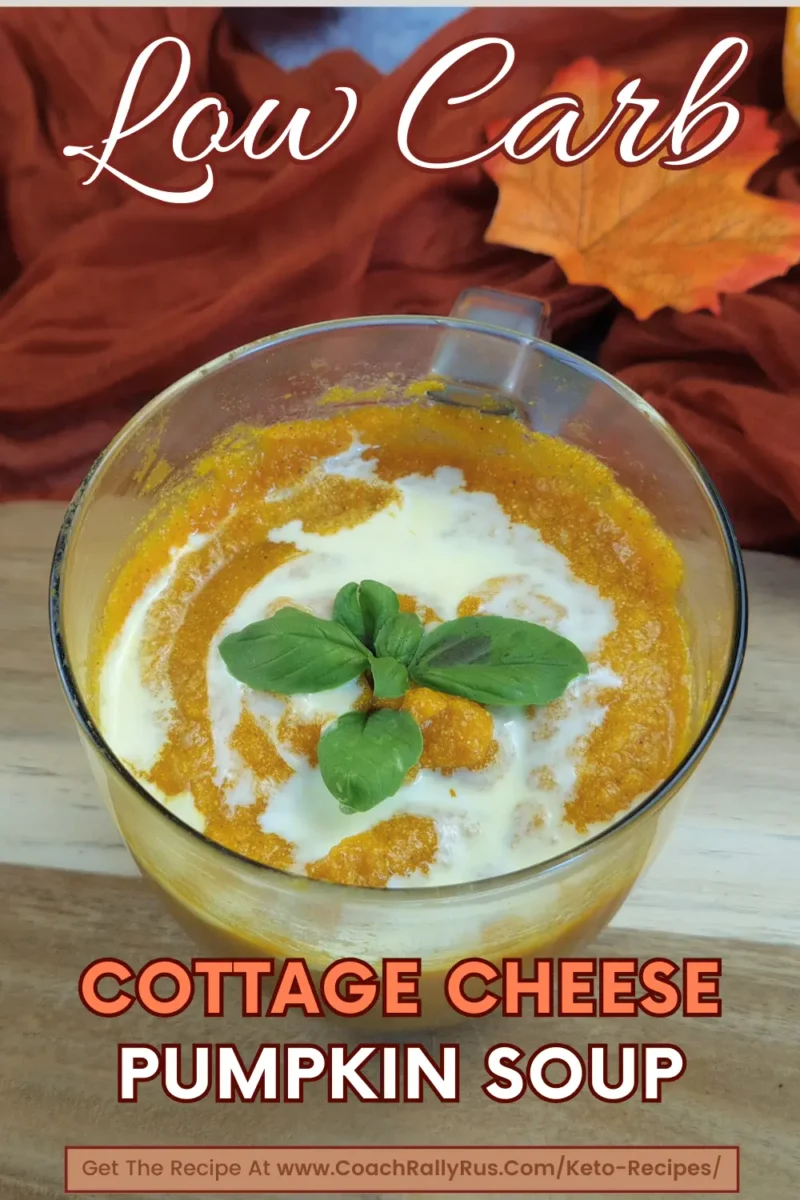 A vibrant orange Cottage Cheese Pumpkin Soup garnished with fresh basil in a clear glass cup, set against a wooden background with an orange cloth. The image has “Low Carb” written in cursive at the top and includes the text “Cottage Cheese Pumpkin Soup” at the bottom.