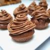 Close-up of six chocolate cupcakes topped with a swirl of rich chocolate cream cheese frosting, displayed on a white surface.