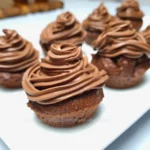 Close-up of six chocolate cupcakes topped with a swirl of rich chocolate cream cheese frosting, displayed on a white surface.