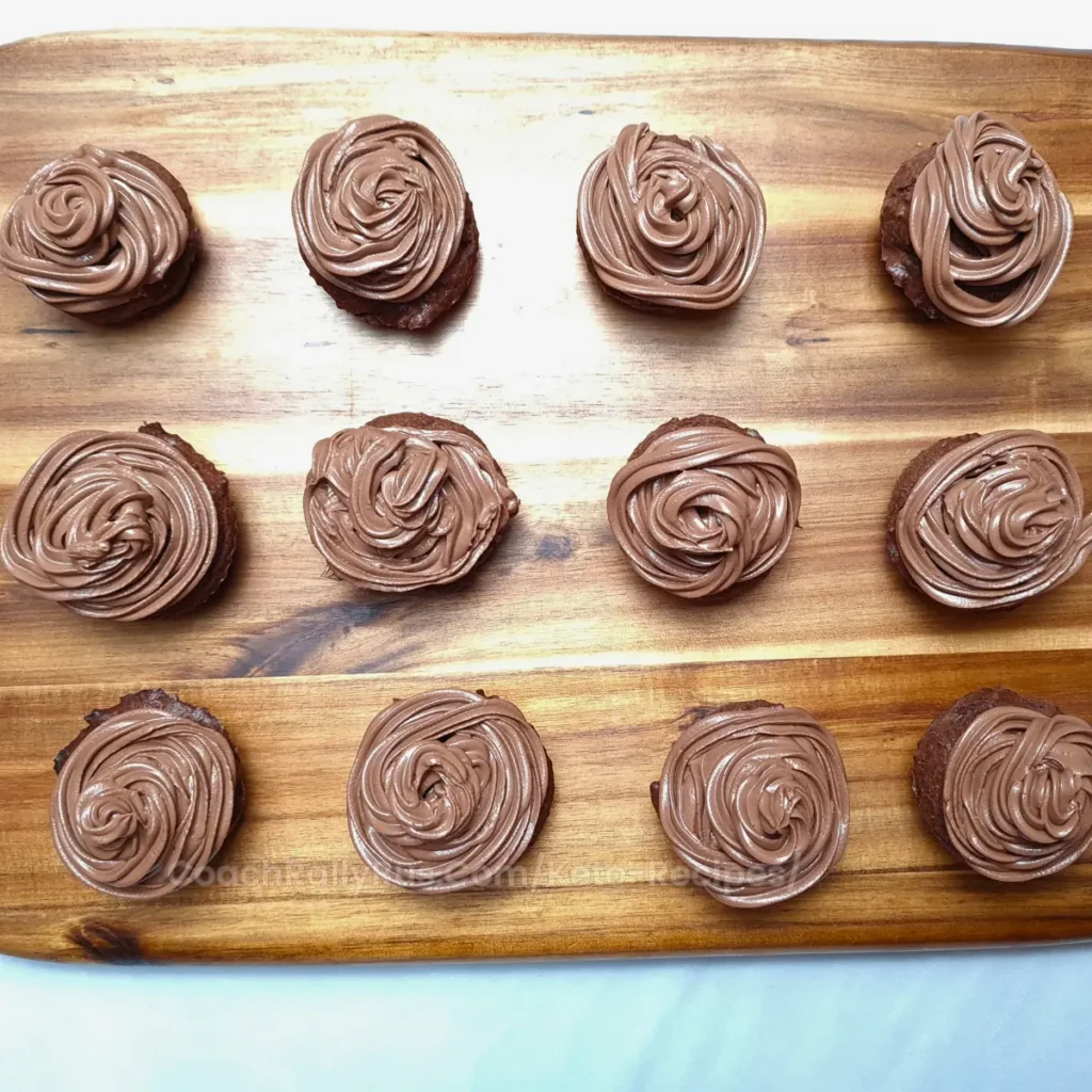 A dozen chocolate cupcakes with swirls of rich chocolate cream cheese frosting, neatly arranged in rows on a wooden board.