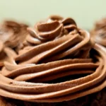 Close-up of a rich, creamy chocolate frosting piped in a swirling pattern atop cupcakes, indicative of a keto-friendly recipe.