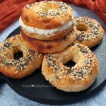 A stack of golden-brown cottage cheese bagels topped with various seeds on a plate.