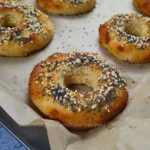 A freshly baked Keto Cottage Cheese Bagel with a golden-brown crust, sprinkled with a mix of white and black sesame seeds, poppy seeds, and sea salt flakes on top.