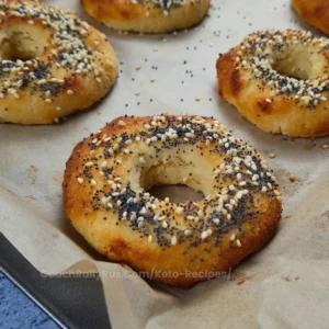 A freshly baked Keto Cottage Cheese Bagel with a golden-brown crust, sprinkled with a mix of white and black sesame seeds, poppy seeds, and sea salt flakes on top.