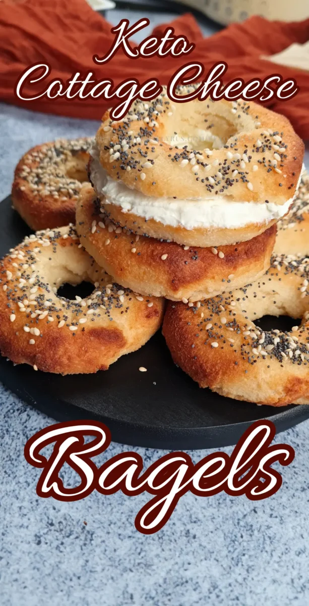 High Protein Keto Cottage Cheese Bagels A stack of three golden-brown Keto Cottage Cheese Bagels topped with cream cheese and sprinkled with everything bagel seasoning, displayed on a black plate against a blurred background.