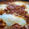 Close-up of a keto shakshuka with poached eggs nestled in a rich tomato sauce, sprinkled with green onions.