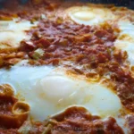 Close-up of a keto shakshuka with poached eggs nestled in a rich tomato sauce, sprinkled with green onions.