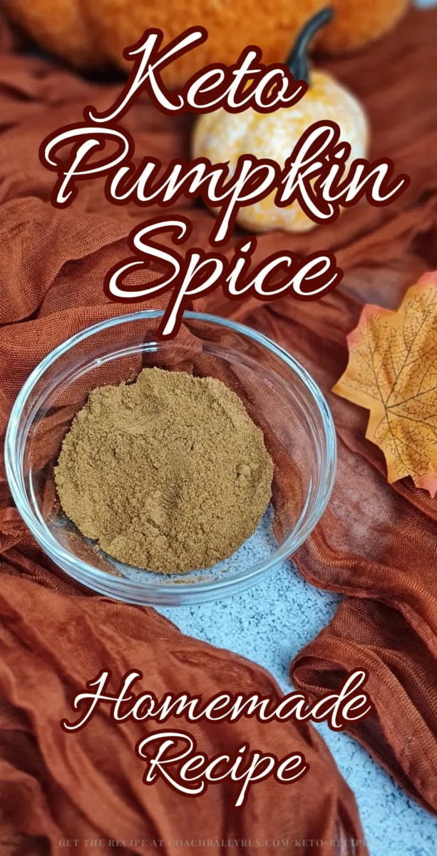 A clear glass bowl filled with a fine, brownish-orange powder labeled as Keto Pumpkin Spice sits atop a crinkled, rust-colored cloth. Surrounding the bowl are autumn leaves and a small pumpkin, evoking a fall theme. The image has text overlay that reads “Keto Pumpkin Spice,” “Homemade Recipe,” and at the bottom “Get the full recipe at www.CoachRallyRus.com/Keto-Recipes.”