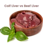 Calf Liver vs Beef Liver comparison displayed with a portion of liver in a round wooden bowl garnished with a basil leaf, against a white background.