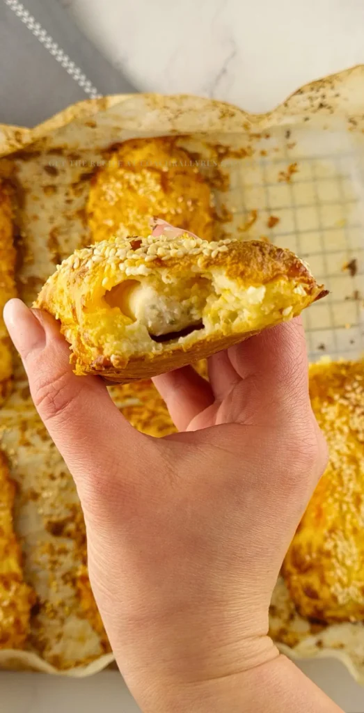 A hand holding a keto sausage roll with a bite taken out, revealing the sausage filling inside.