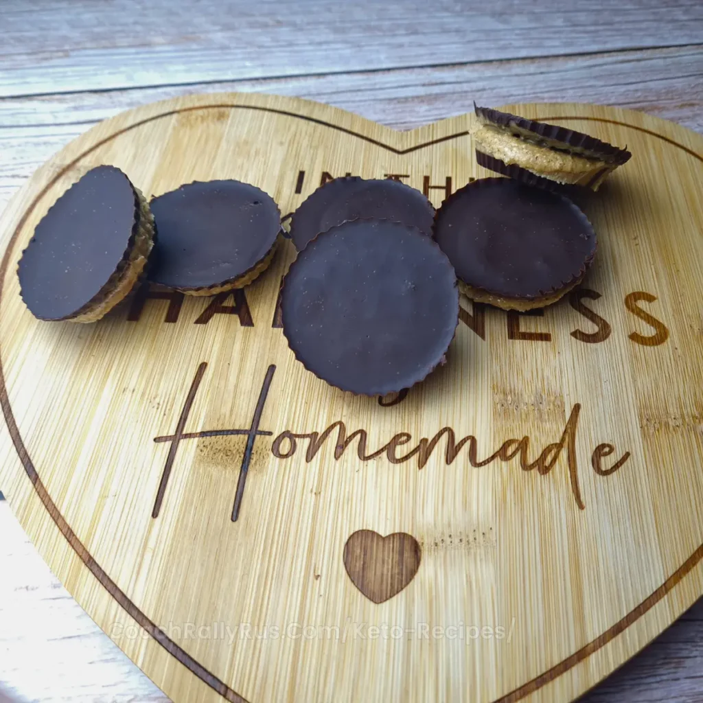 Six keto peanut butter cups arranged on a heart-shaped wooden board