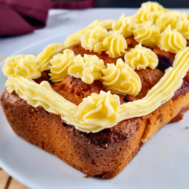 A delicious keto blueberry creme fraiche pound cake topped with intricate swirls of keto Royal Icing Buttercream, presented on a white plate.