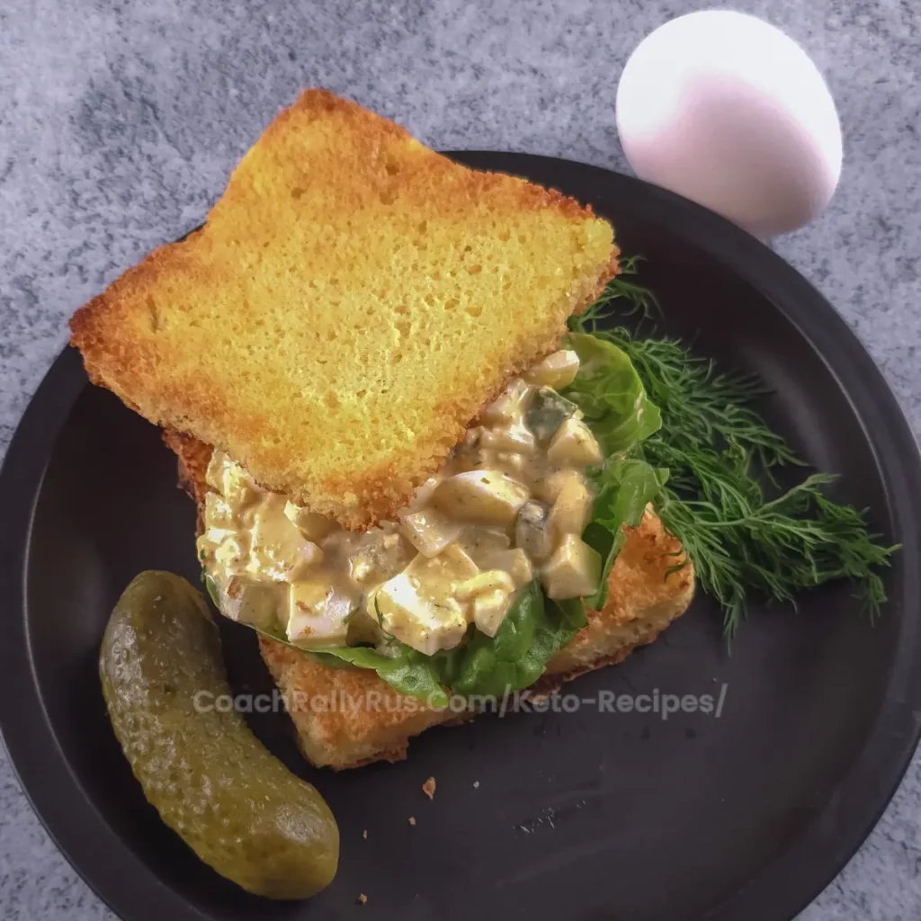 Overhead view of keto cottage cheese dill pickle egg salad served on toasted bread with fresh dill and a whole pickle.