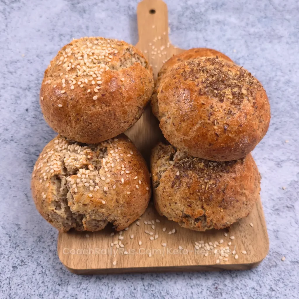 Keto flaxseed cottage cheese bread rolls topped with sesame seeds and flaxseed, freshly baked and arranged on a wooden board.