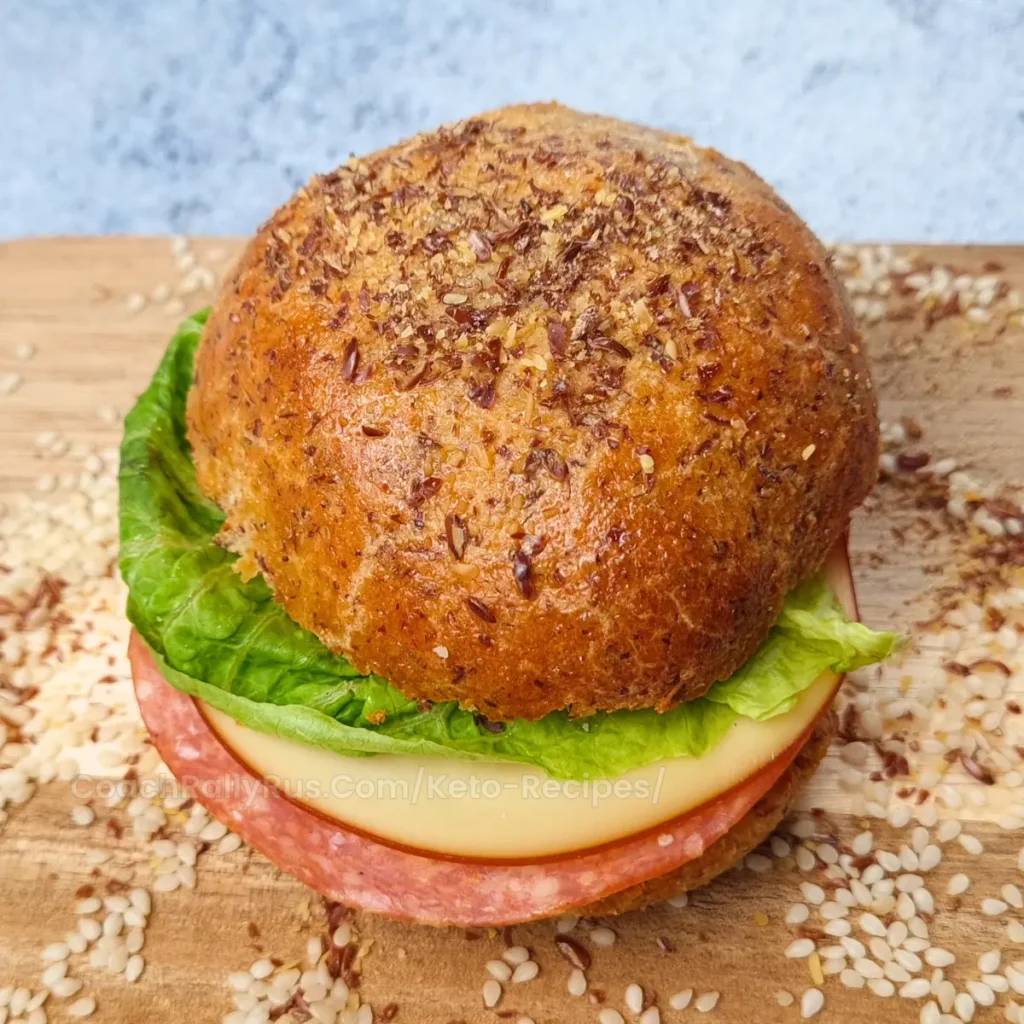 High-protein keto flaxseed cottage cheese bread roll sandwich with lettuce, salami, and cheese on a wooden board.