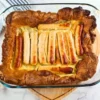 Golden-brown keto toad in the hole with sausages nestled in a fluffy, gluten-free batter baked in a glass baking dish.