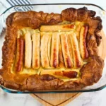 Golden-brown keto toad in the hole with sausages nestled in a fluffy, gluten-free batter baked in a glass baking dish.