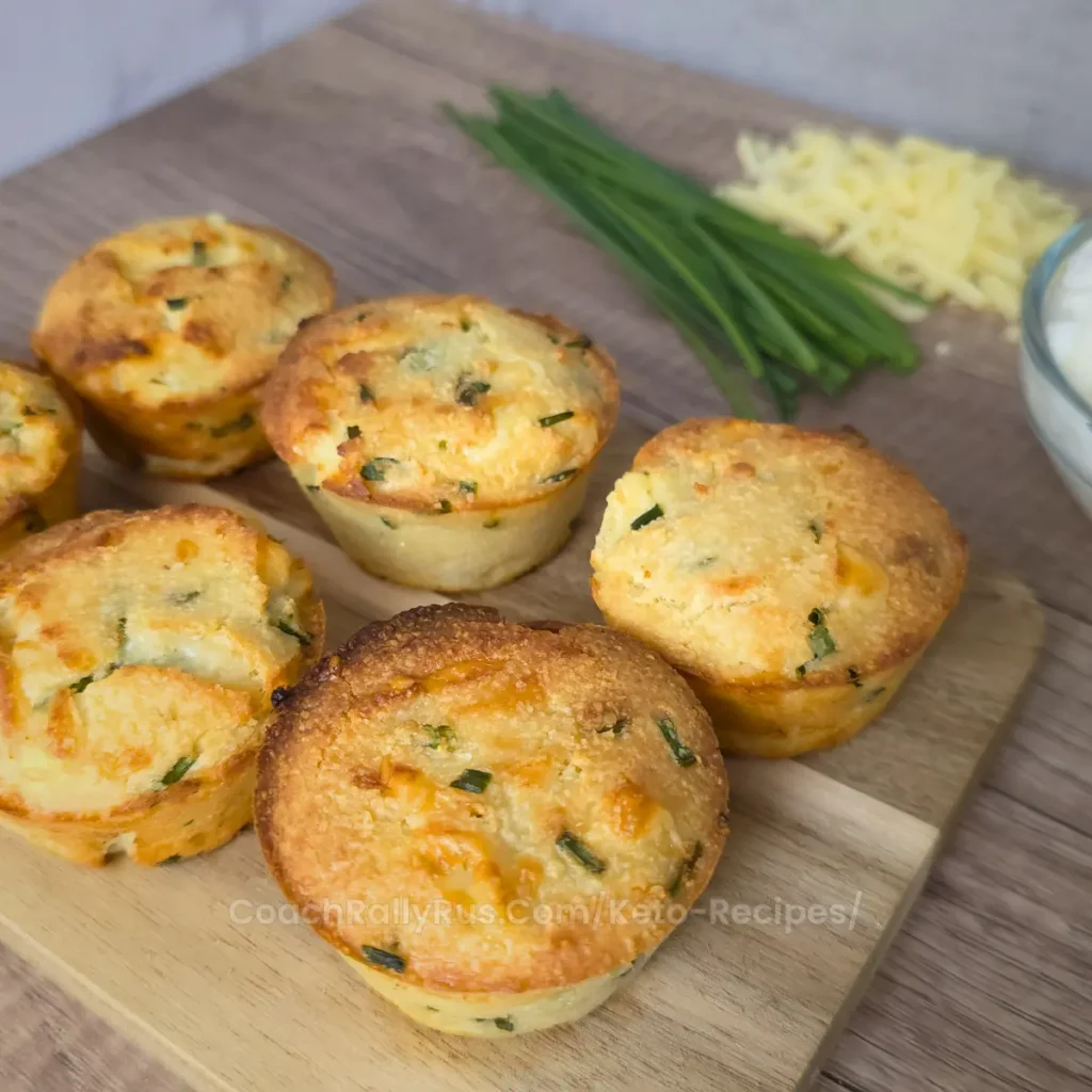 Freshly baked keto cottage cheese dinner biscuits with cheddar and chives on a wooden cutting board.