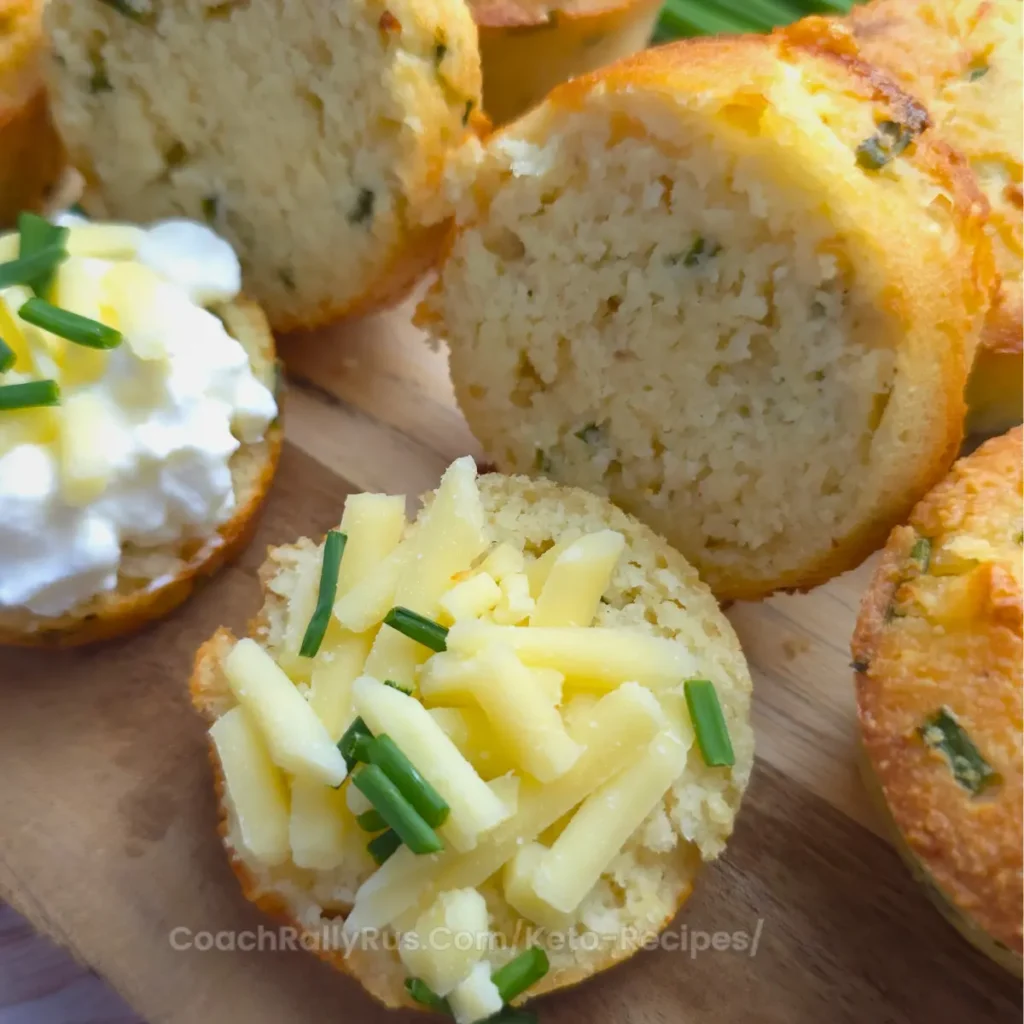 A close-up of a keto biscuit topped with cottage cheese, shredded cheddar, and fresh chives.