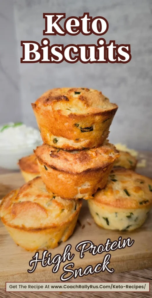 A stack of golden brown keto biscuits with cheddar and chives, labeled as a high-protein snack, with a bowl of cottage cheese in the background.