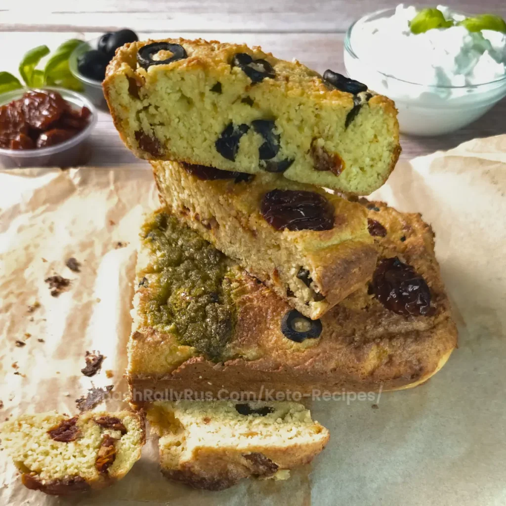 A loaf of sun-dried tomato and olive cottage cheese bread with slices stacked on parchment paper.