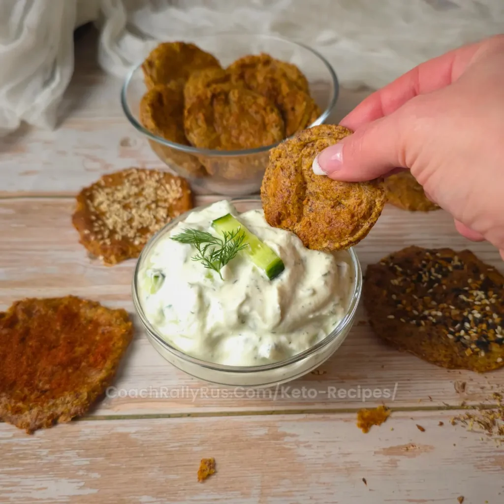 A hand dipping a keto flaxseed cottage cheese chip into a creamy dip.