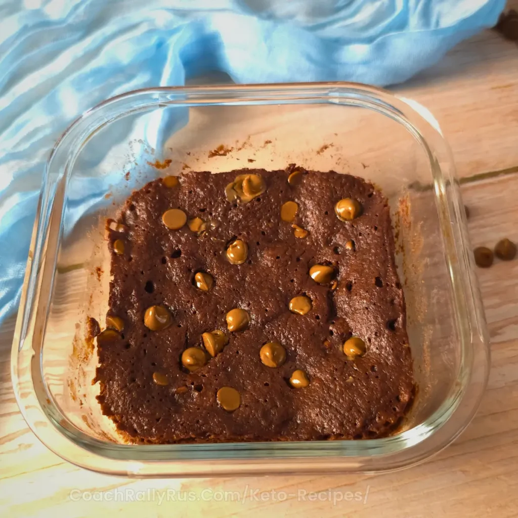 A baked keto cottage cheese brownie in a glass dish with chocolate chips.
