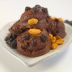 Chocolate peanut butter cookie dough made with cottage cheese, styled in playful scoops on a white dish, garnished with roasted peanuts and chocolate chips