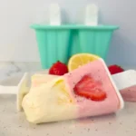 Strawberry lemonade cottage cheese popsicles on marble background with mold and fruit.